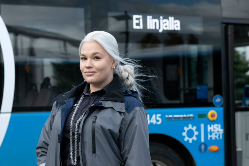 Linja-autonkuljettaja seisoo takki päällään linja-auton edustalla.