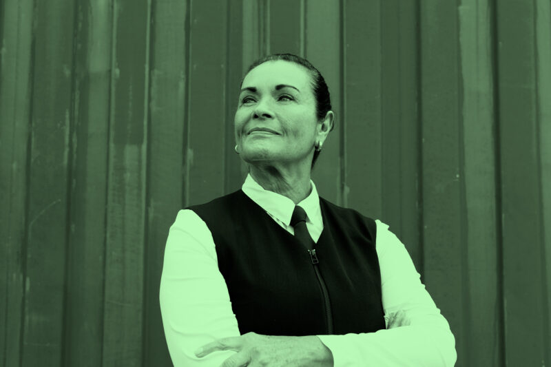 A bus driver stands with arms crossed in front of a wall, looking upwards.