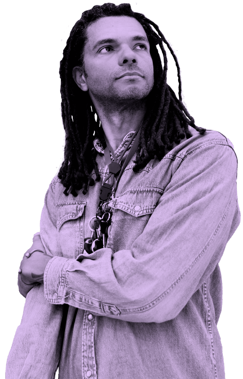 A youth worker with dreadlocks stands and looks up to the right.