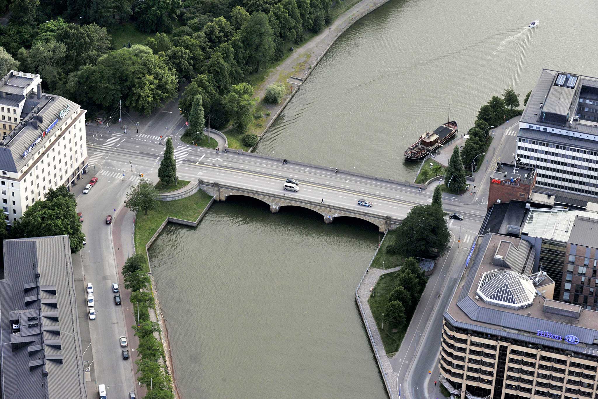 An aerial view showing an old bridge, a bay, a park, and apartment buildings by the seashore.