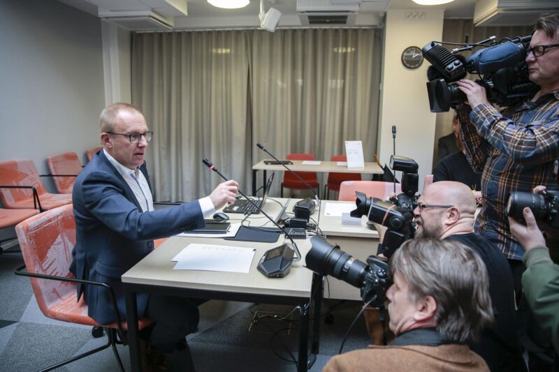 FFC:s ordförande Jarkko Eloranta sitter vid ett bord och framför honom står ett stort antal fotografer med tv- och filmkameror.