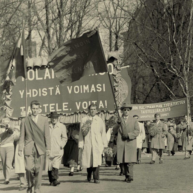 Folk håller upp stora banderoller flaggor i första maj-tåget 1956.